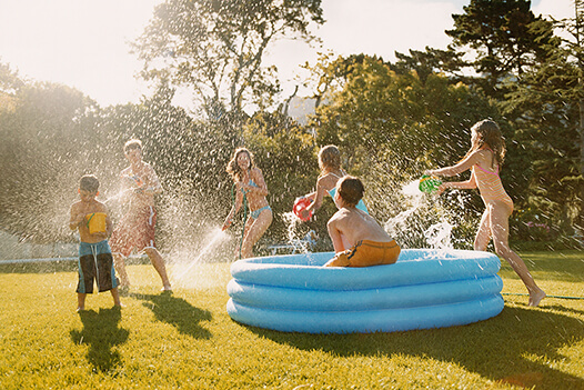 kids playing in a blow up pool outside with water guns