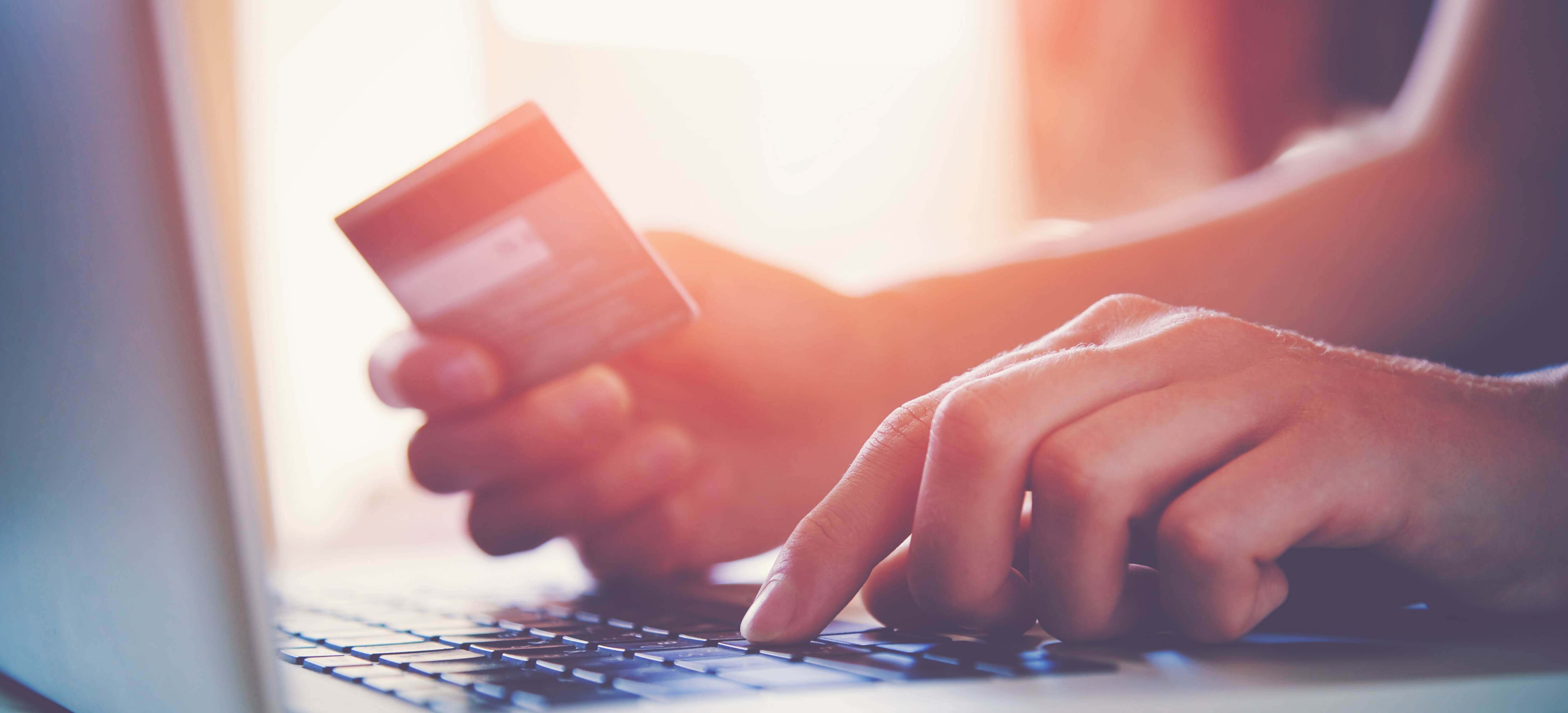 Hand holding credit card above laptop computer keyboard