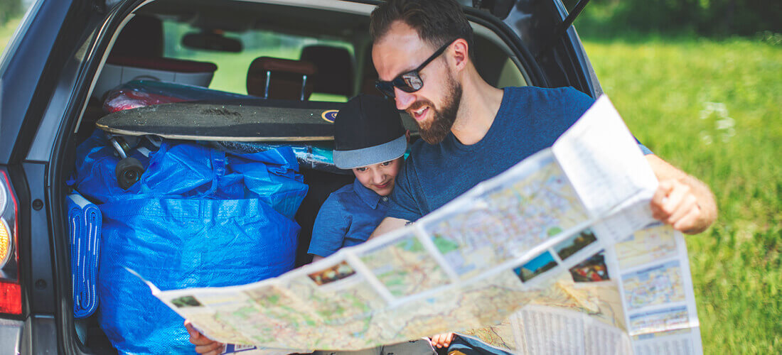 man and child sit at back of car looking at map